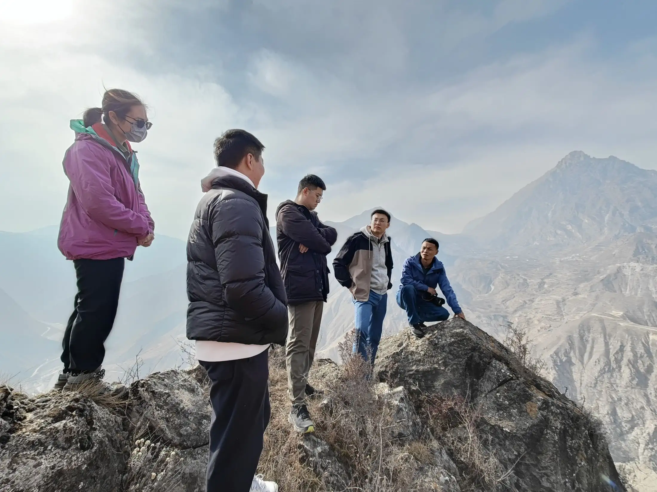 Five group members on a rocky ridge looking out over a volcanic slope disappearing into cloud.