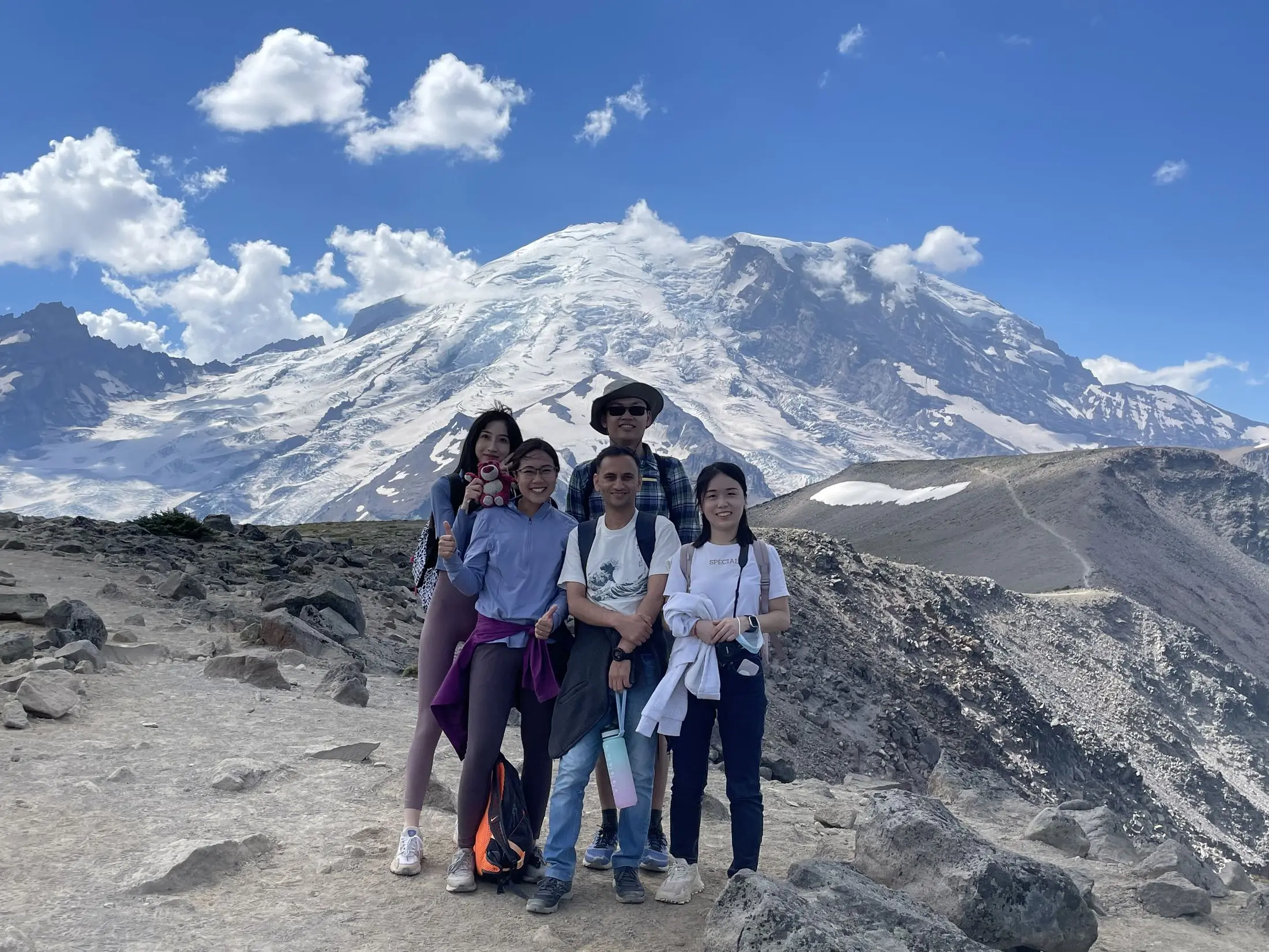 Five group members on a bare pumice slope with a snow-covered volcanic summit rising behind them.