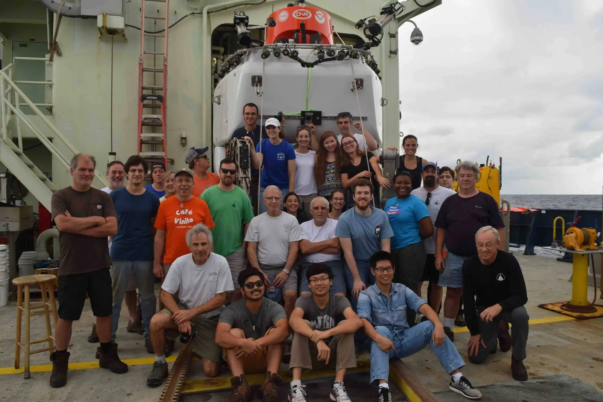 A large science party posed in front of the open hangar doors of the submersible Alvin aboard its support ship.