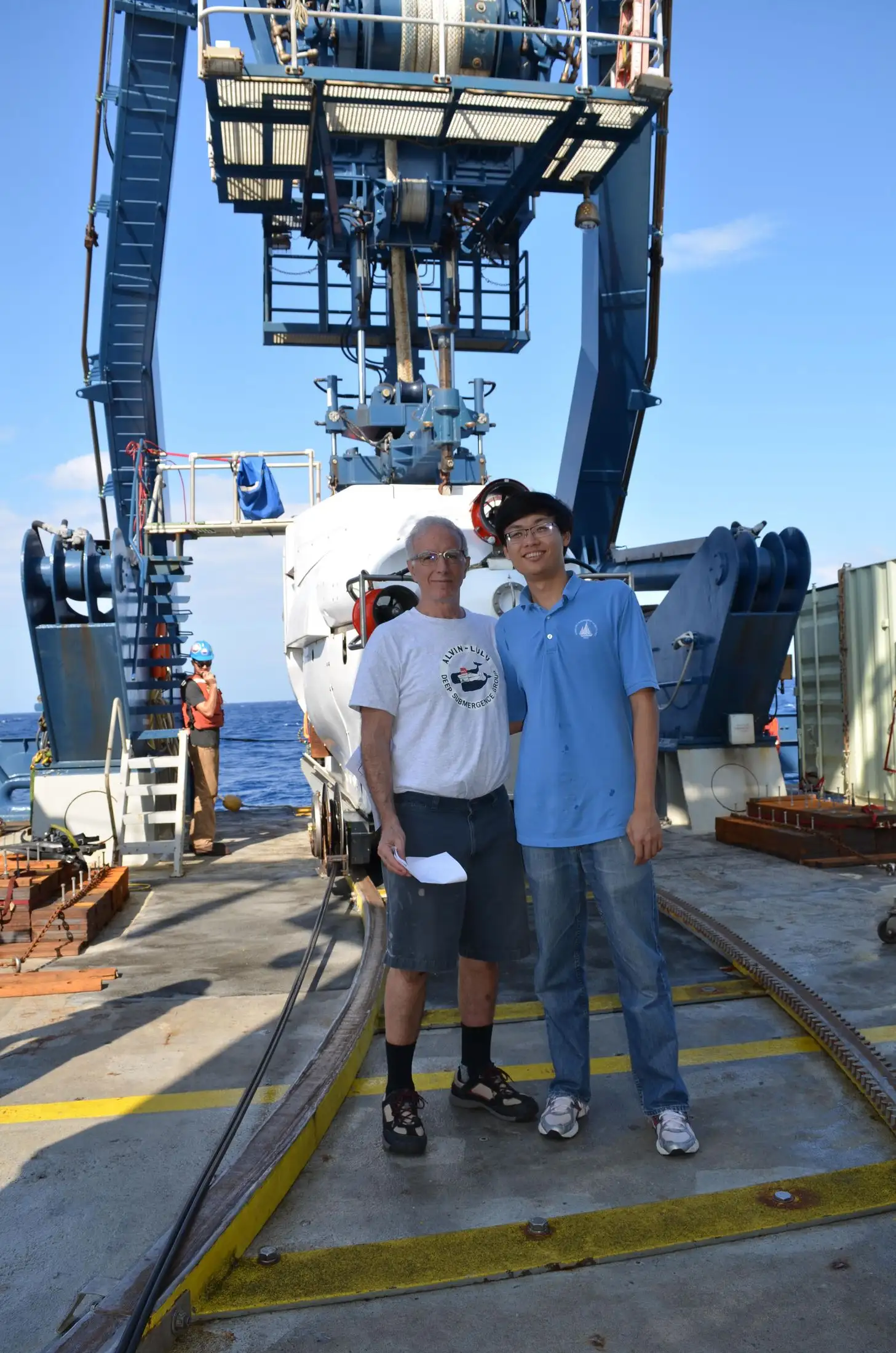 Two researchers standing on a ship deck beside the deep-submergence vehicle Alvin under its launch gantry.
