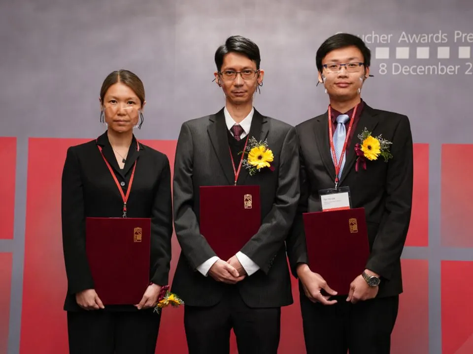 Three CUHK scholars holding award folders on stage at the Croucher Awards presentation; Professor Yen Joe Tan is on the right.